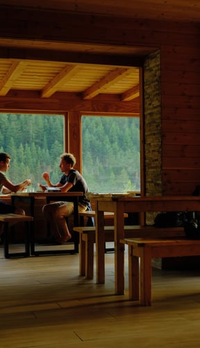 Two guests at a wooden table with a forest view through large windows