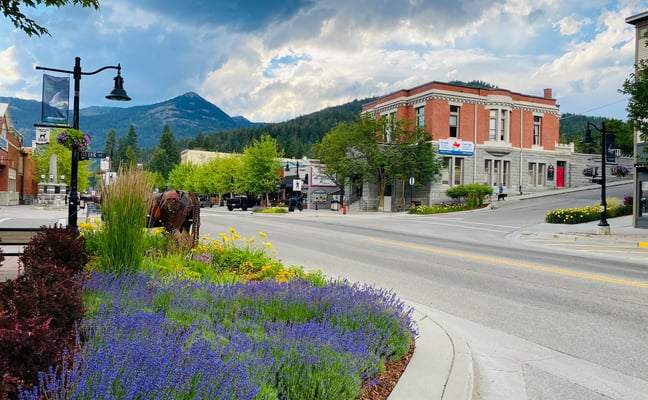 Rossland's Queen Street on a summer day, lavender in bloom along the median with brick storefronts and a mountain behind